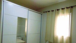 A bedroom with a sliding closet door, a bed, and a window with curtains. - Flats Aconchegantes (Campos do Jordão)