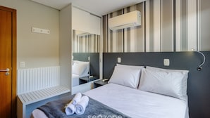 Hotellihuone, jossa on sänky, yöpöydät, peili, seinälle asennettu ilmastointilaite ja ovi.