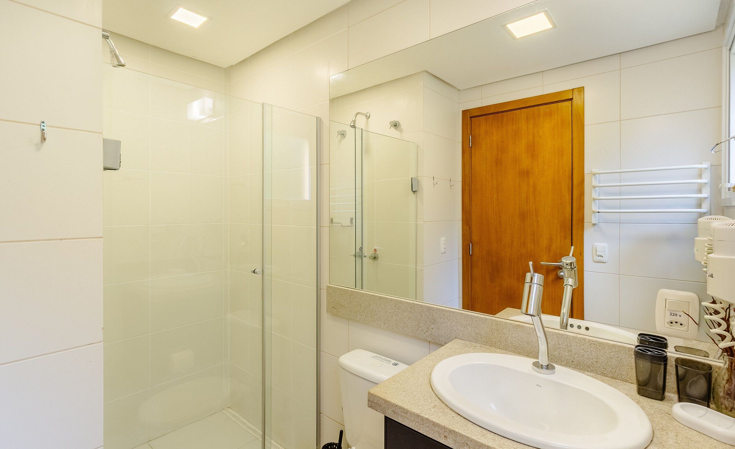 Un bany modern amb una dutxa amb mampara de vidre, un lavabo blanc i una porta de fusta.