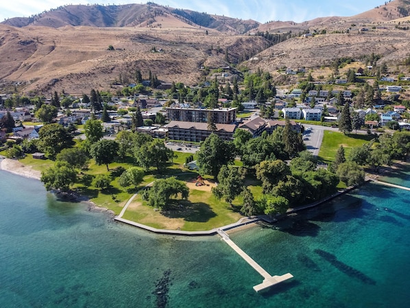 Aerial view of the waterfront park and dock, backed by a resort building and arid hills.
