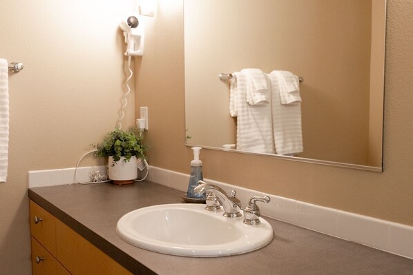 A bathroom vanity featuring an oval sink, large mirror, and wall-mounted hair dryer.