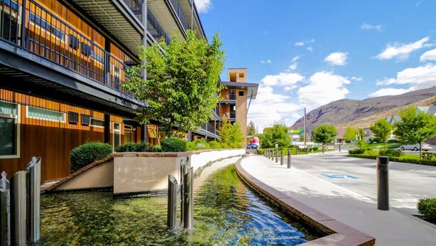 A modern building with a water feature in front, surrounded by greenery and a clear sky.