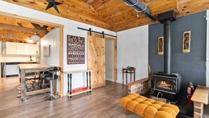 A cozy interior with a wooden ceiling, a central table with bar stools, a sofa, and a wood-burning stove. - Charming Cottage on the Lake - Family and Pet Friendly (LaBelle)