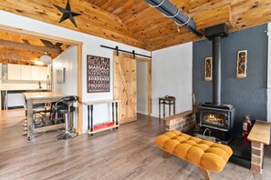 Een gezellig interieur met een houten plafond, een centrale tafel met barstoelen, een bank en een houtkachel.