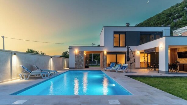 A modern house with a swimming pool, outdoor seating, and a view of the hills.