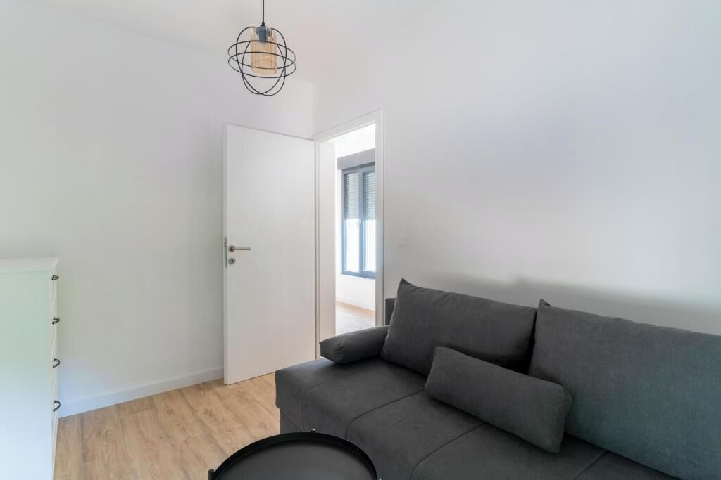 A modern, minimalist room with a grey sofa, a white cabinet, and a hanging light fixture.