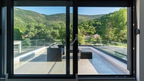 A modern room with a large sliding glass door leading to a balcony with a view of a green hillside.