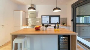 A modern kitchen with a central island, pendant lighting, a built-in wine cooler, and a view through a glass door.