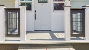 Puerta blanca con un pequeño ventanal encima, flanqueada por dos portones con barrotes de metal.