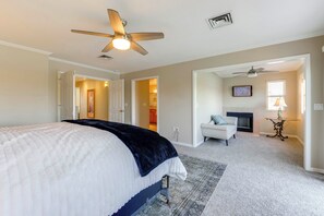 A bedroom with a bed, a ceiling fan, a fireplace, and a hallway leading to other rooms.