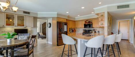 A modern kitchen with a central island, bar stools, and a dining table with chairs.