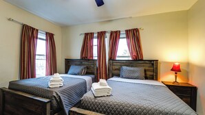 A hotel room with two beds, a wooden headboard, a nightstand with a lamp, and a window with curtains.