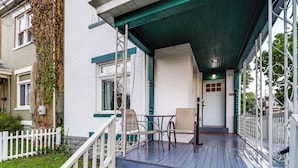 A wooden deck with outdoor furniture, a white picket fence, and a building with white walls and green trim.
