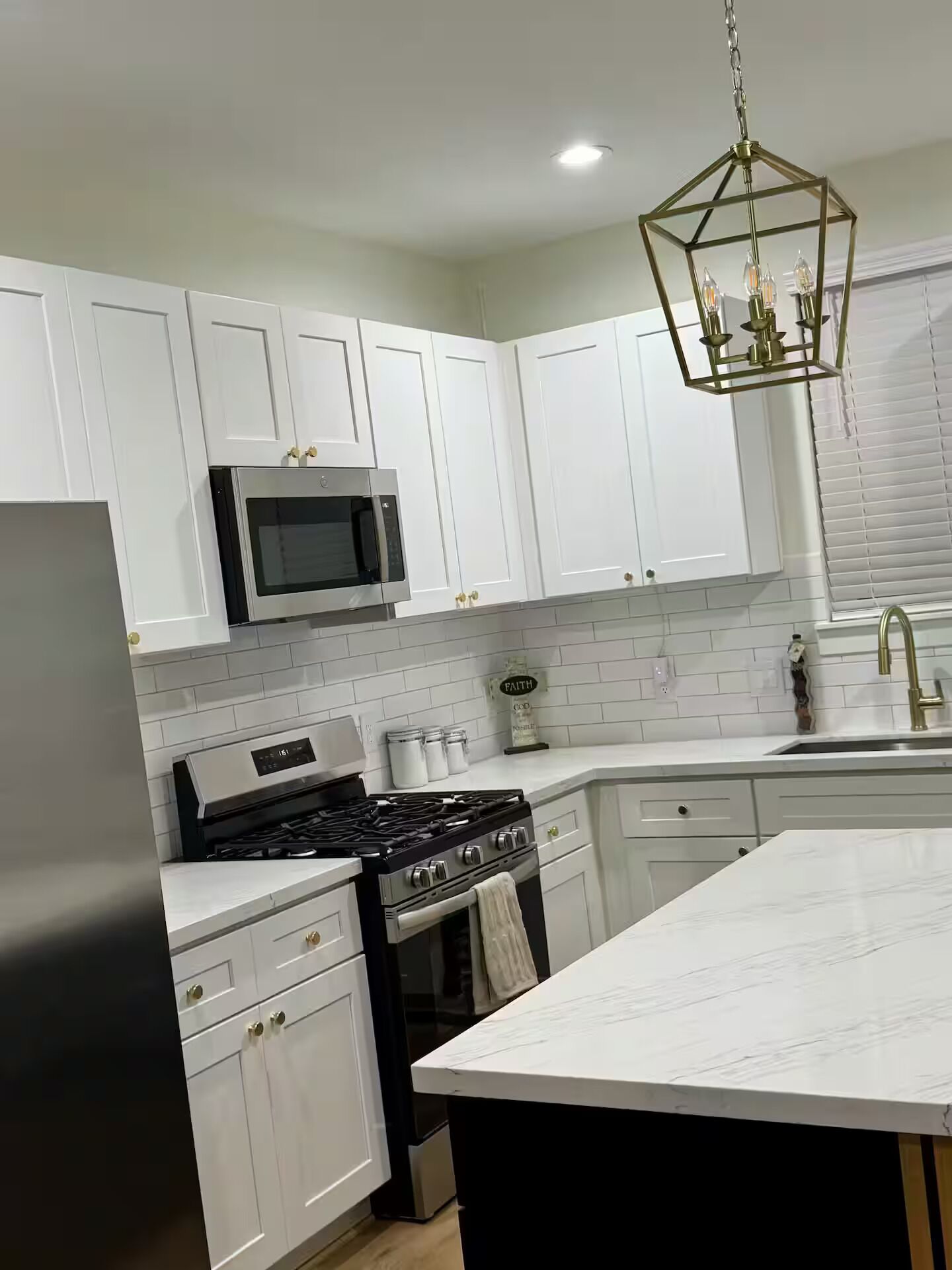 A modern kitchen with white cabinets, a stainless steel refrigerator, a microwave, a gas stove, and a large island with a marble countertop.