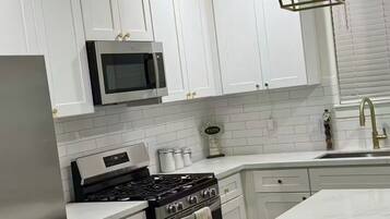 A modern kitchen with white cabinets, a stainless steel refrigerator, a microwave, a gas stove, and a large island with a marble countertop.