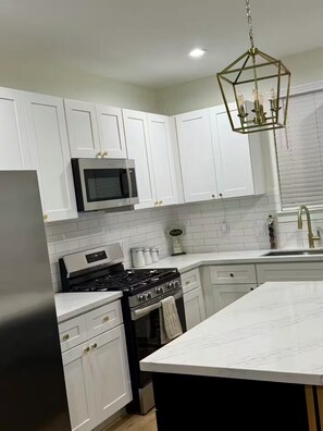 A modern kitchen with white cabinets, a stainless steel refrigerator, a microwave, a gas stove, and a large island with a marble countertop. - Houston Haven near all you need /A/ (Houston)