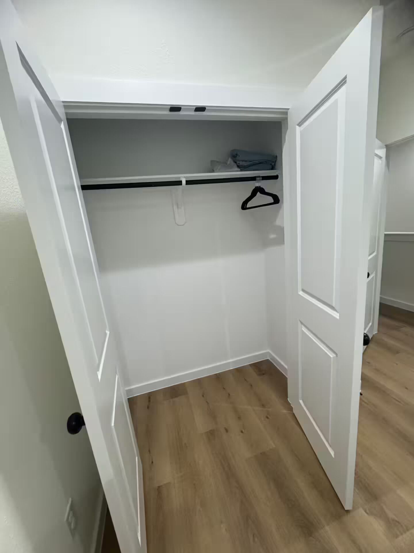 A walk-in closet with a wooden floor, white walls, and a hanging rod.