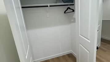 A walk-in closet with a wooden floor, white walls, and a hanging rod.