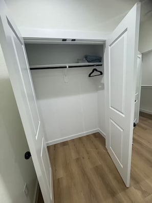 A walk-in closet with a wooden floor, white walls, and a hanging rod. - Houston Haven near all you need /A/ (Houston)