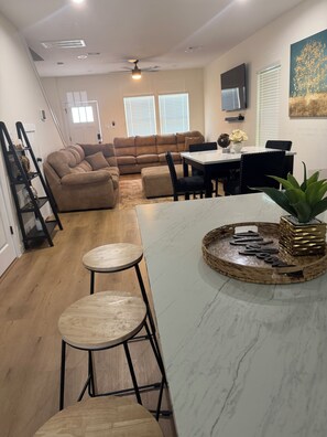 A modern kitchen with a marble countertop, two stools, a dining table with chairs, and a ceiling fan. - Houston Haven near all you need /A/ (Houston)