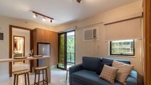 A modern living room with a blue sofa, wooden stools, a kitchen area with a dining table, and a sliding glass door leading to a balcony. - 6 Minutes From Leblon Beach Gsm103 (Rio de Janeiro)