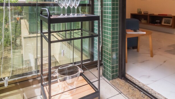 A modern living room with a glass door leading to a balcony, a TV mounted on the wall, and a small wooden table. - 6 Minutes From Leblon Beach Gsm103 (Rio de Janeiro)
