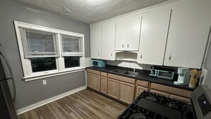 A compact kitchen with a gas stove, a microwave, and wooden cabinets. - Mid-Century Tudor in Quiet Detroit Neighborhood (Detroit)