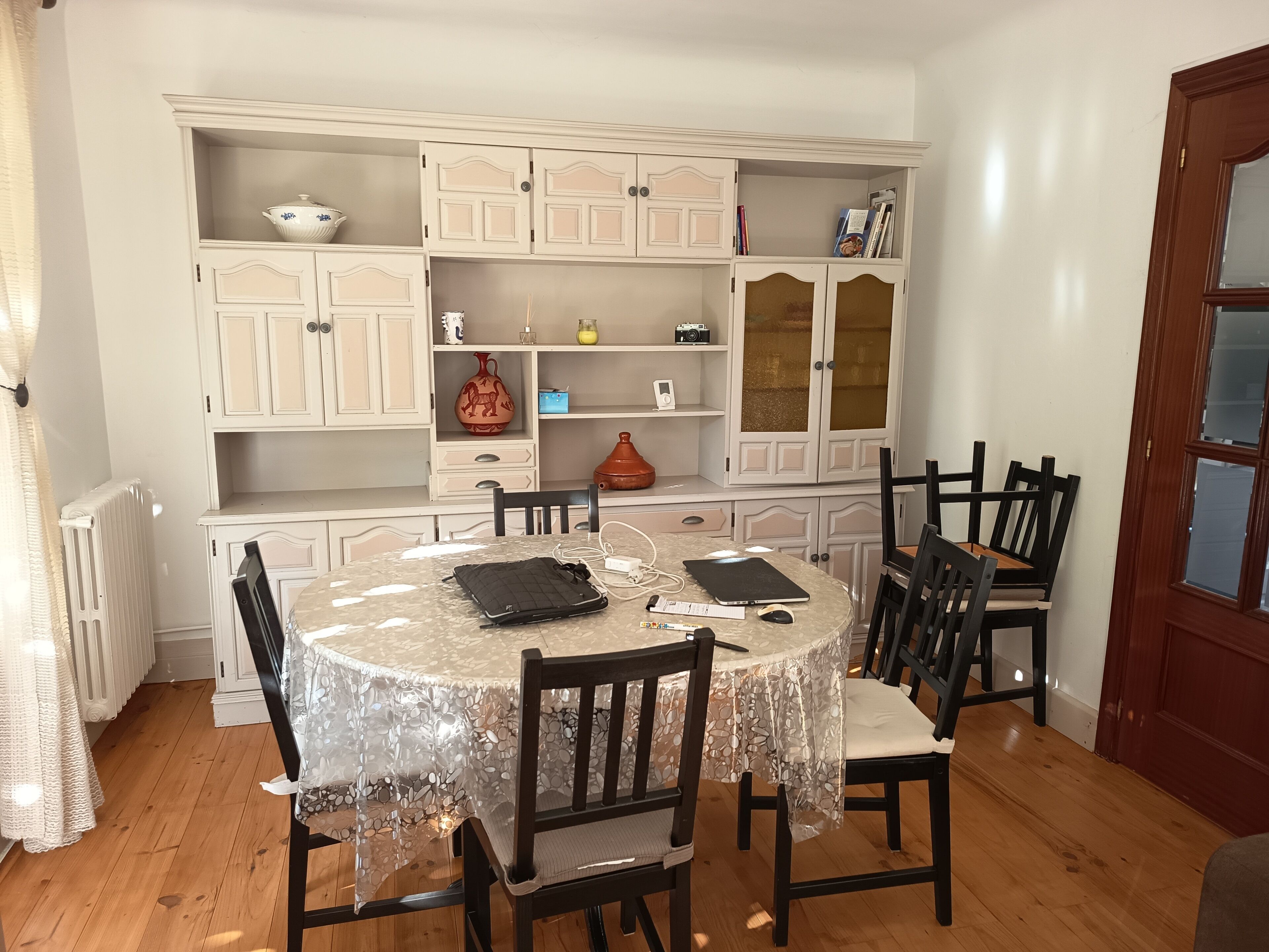 A dining area with a round table, chairs, and a white cabinet with shelves.