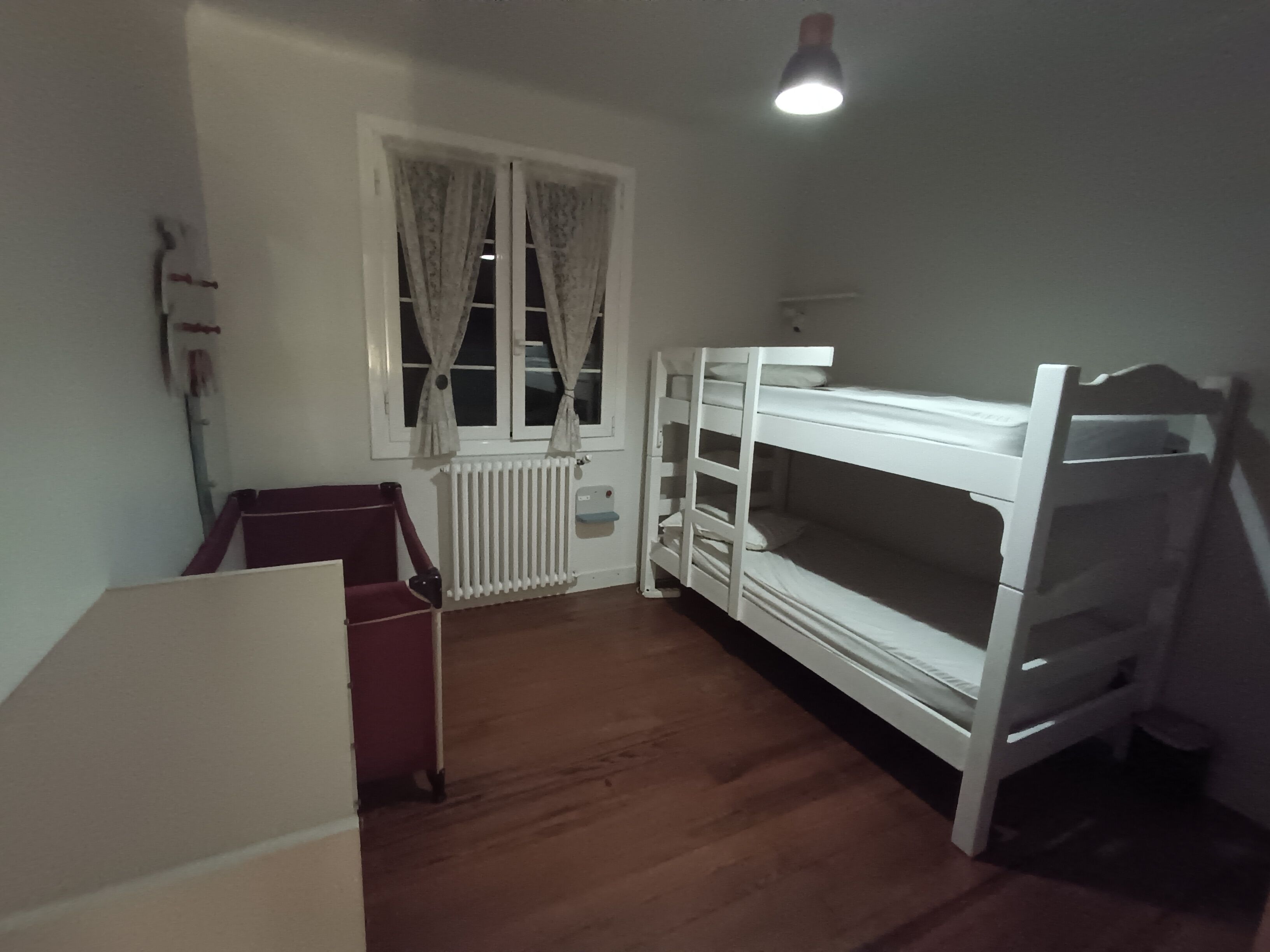Une chambre avec un lit superposé, un radiateur, une fenêtre avec des rideaux et un bureau.