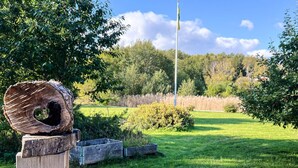 A wooden post with a log sculpture, a flagpole, and a grassy field with trees in the background. - 5 Person Holiday Home in Adelso (Adelso)
