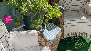 A wicker sofa with striped cushions, a checkered tablecloth, a potted plant, and a basket on a green surface. - 5 Person Holiday Home in Adelso (Adelso)