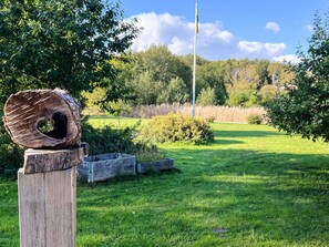A wooden post with a log sculpture, a flagpole, and a grassy field with trees in the background. - 5 Person Holiday Home in Adelso (Adelso)