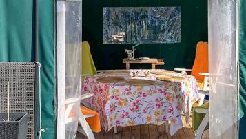 A covered outdoor dining area with a table set for two, surrounded by chairs, and a painting on the wall.
