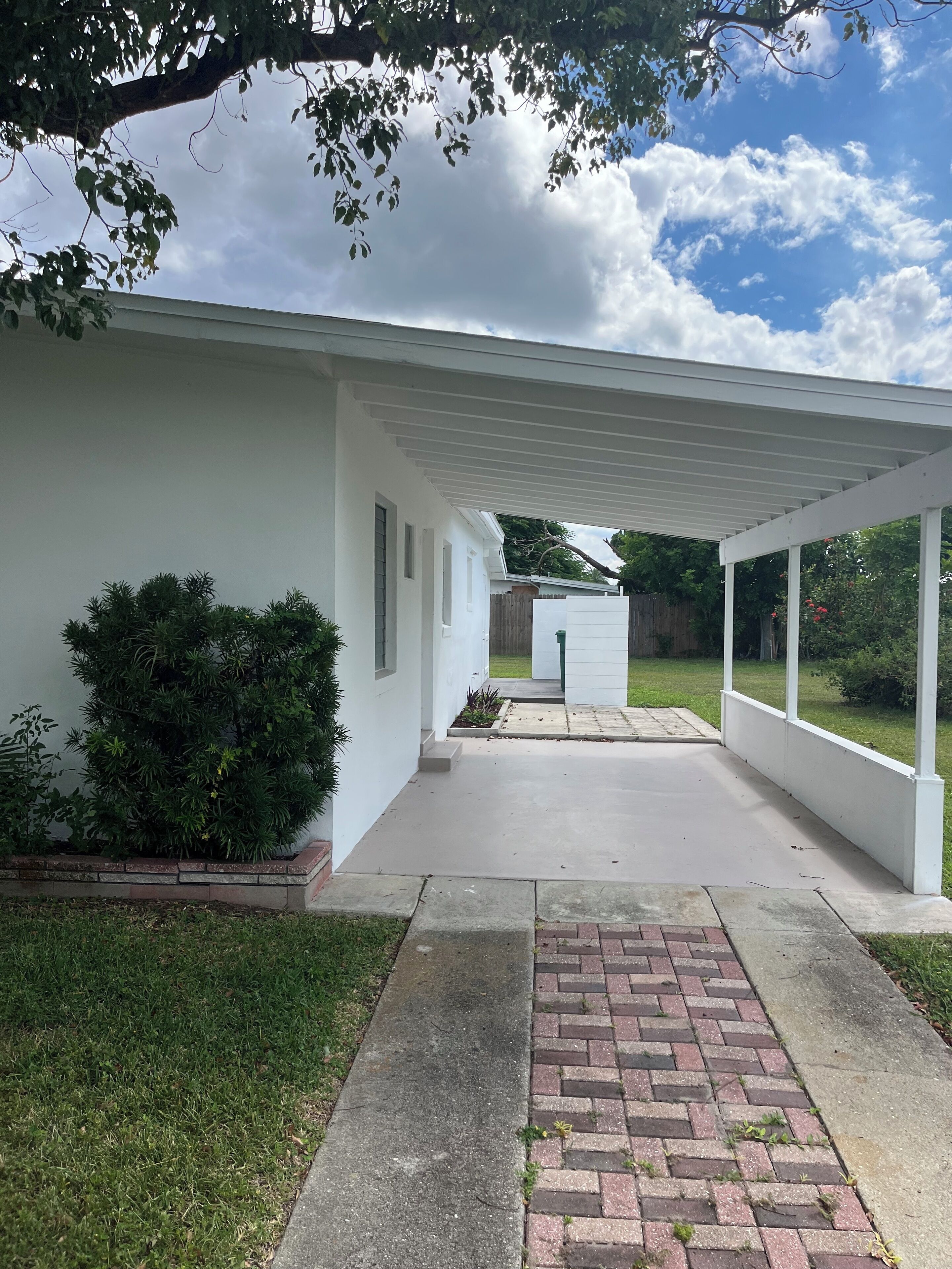 A covered patio area with a concrete walkway leading to a white building.