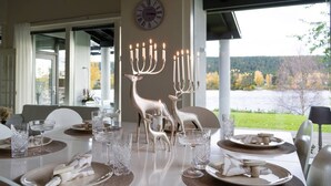 Een eettafel gedekt met kaarsen, glazen en borden, met uitzicht op een meer en bos in de achtergrond.