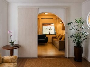 A room with a sliding door leading to a living area, a round table with a vase, a potted plant, and a sofa.