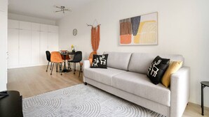 Un salon moderne avec un canapé gris, des fauteuils orange et noirs, une table à manger et un grand tableau abstrait accroché au mur.
