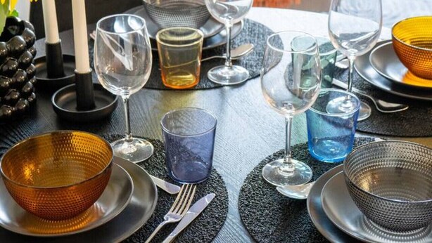 Une table à manger dressée avec différents types de verres et d’assiettes, entourée d’un salon moderne avec un canapé et des coussins.
