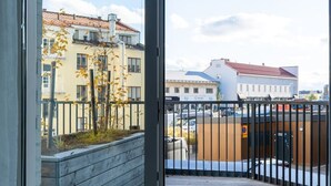 Une vue depuis un balcon doté d’une terrasse en bois, donnant sur un quartier résidentiel avec ses immeubles et un ciel dégagé.