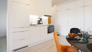Une cuisine moderne avec des meubles blancs, une machine à café et un coin repas avec une table dressée pour deux personnes.