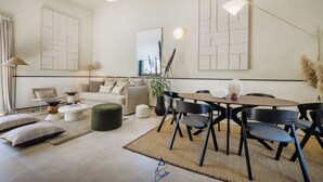 A modern living room with a sofa, ottoman, dining table, and chairs. There are abstract wall art pieces and a large window. - Charming New 3BR Villa for 6+2 with Private Pool (Višnjan)