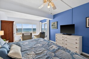 A bedroom with a bed, a TV, a dresser, and a view of the ocean.