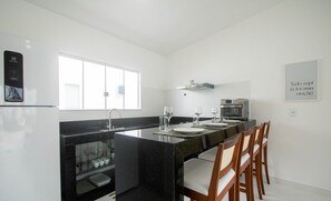 A modern kitchen with a black marble island, white walls, and a window providing natural light. - Fully Equipped Apartments in a Condo With a Pool, 750m From the Beach - Vifs (Porto Seguro)