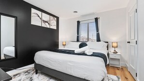 Een moderne slaapkamer met een groot bed, nachtkastjes met lampen, een spiegel en kunst aan de muur.