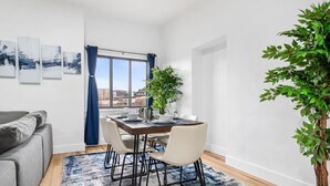 Een moderne eetruimte met een houten tafel gedekt voor vier personen, een grijze bank en een groot raam met blauwe gordijnen.
