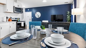 A modern dining area with a round table set for four, white plates, clear glasses, and a small potted plant. - Cozy King Suite|Central, Workspace + Free Parking (Pittsburgh)