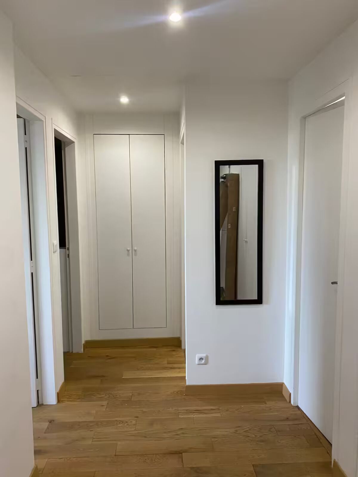 A hallway with wooden flooring, white walls, and a wardrobe with two doors.