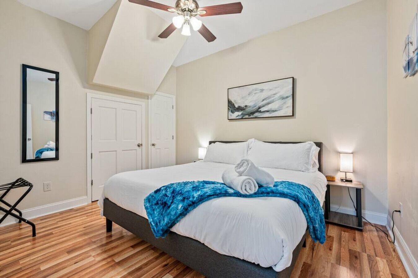 Une chambre à coucher avec un lit, un ventilateur de plafond, un tableau, une table de chevet et une chaise.