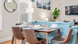 Un comedor con una mesa dispuesta para cuatro personas, un sofá, un televisor y un espejo.