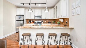 Una cocina moderna con gabinetes blancos, encimera de granito y cuatro taburetes de bar.